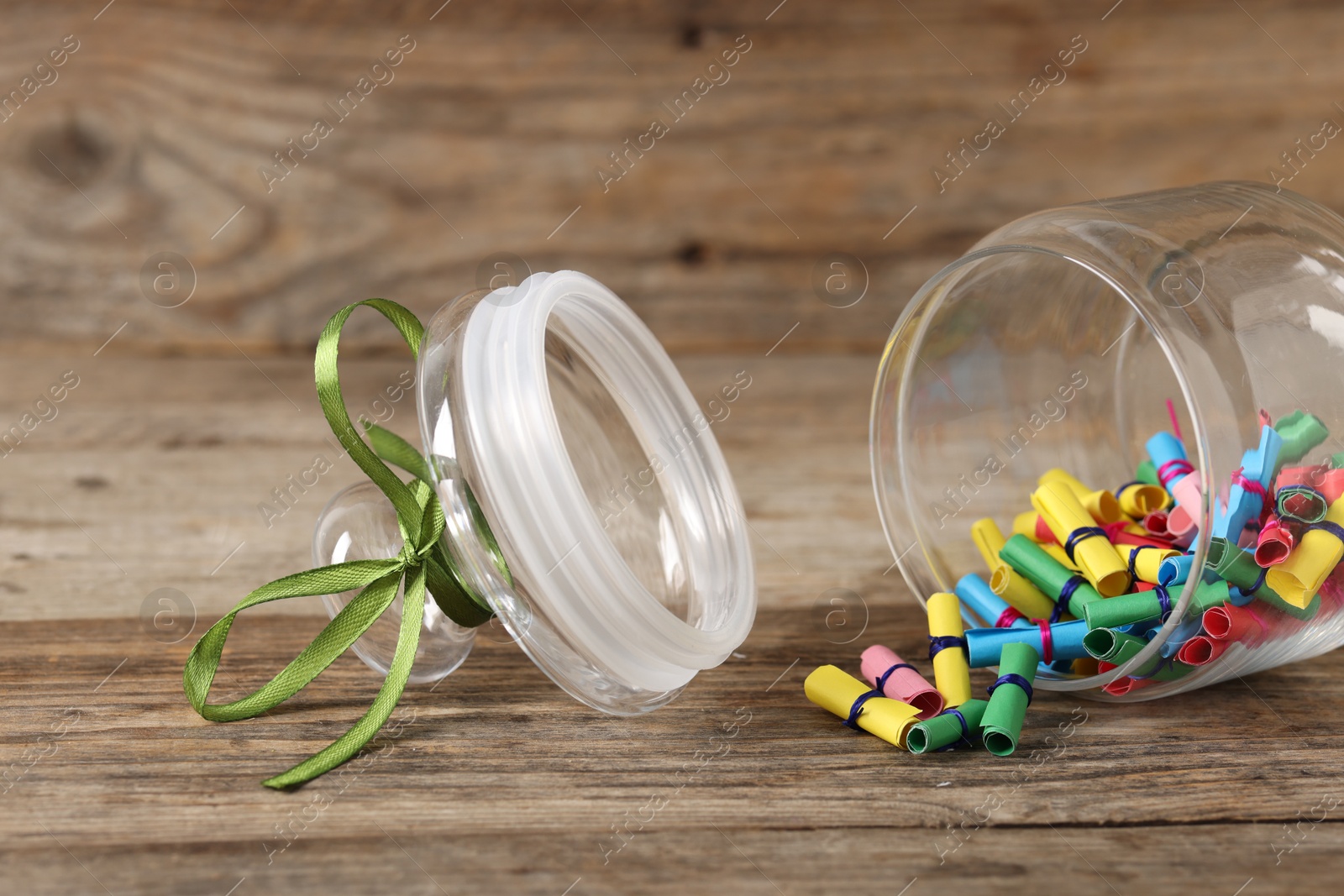 Photo of Colorful paper pieces in glass jar on wooden table, closeup. Notes with messages
