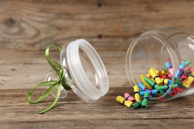 Photo of Colorful paper pieces in glass jar on wooden table, closeup. Notes with messages