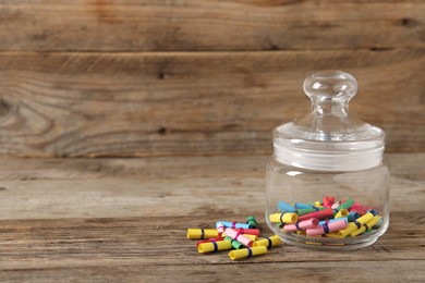 Photo of Colorful paper pieces in glass jar on wooden table, space for text. Notes with messages