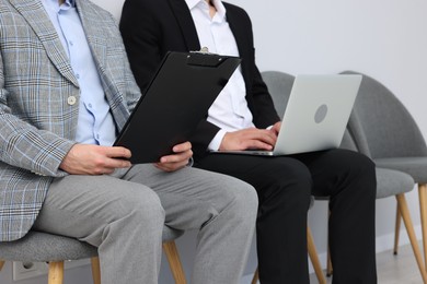 Photo of People waiting in queue on chairs indoors, closeup