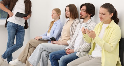 Photo of People waiting in queue on chairs indoors, closeup