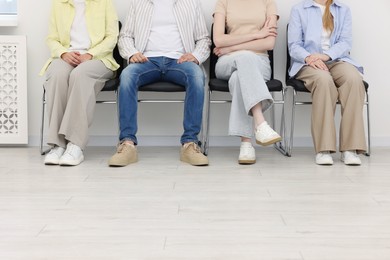 Photo of People waiting in queue on chairs indoors, closeup