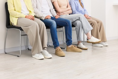Photo of People waiting in queue on chairs indoors, closeup