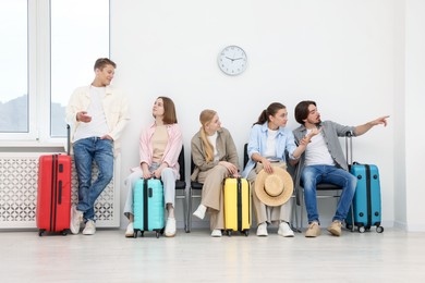 Photo of People with luggages waiting in queue on chairs indoors