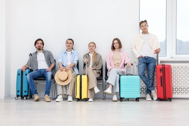 Photo of People with luggages waiting in queue on chairs indoors