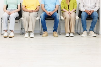 Photo of People waiting in queue on chairs indoors, closeup