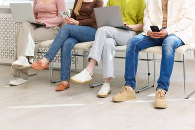 Photo of People with different devices waiting in queue on chairs indoors, closeup