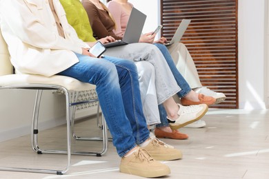 Photo of People with different devices waiting in queue on chairs indoors, closeup