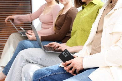 Photo of People with different devices waiting in queue on chairs indoors, closeup