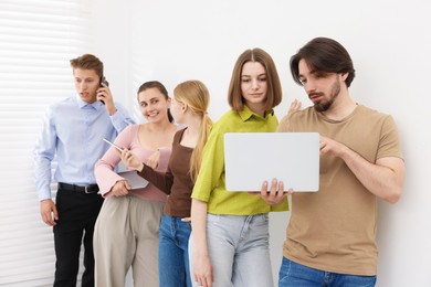 Photo of People with different devices waiting in queue near white wall indoors