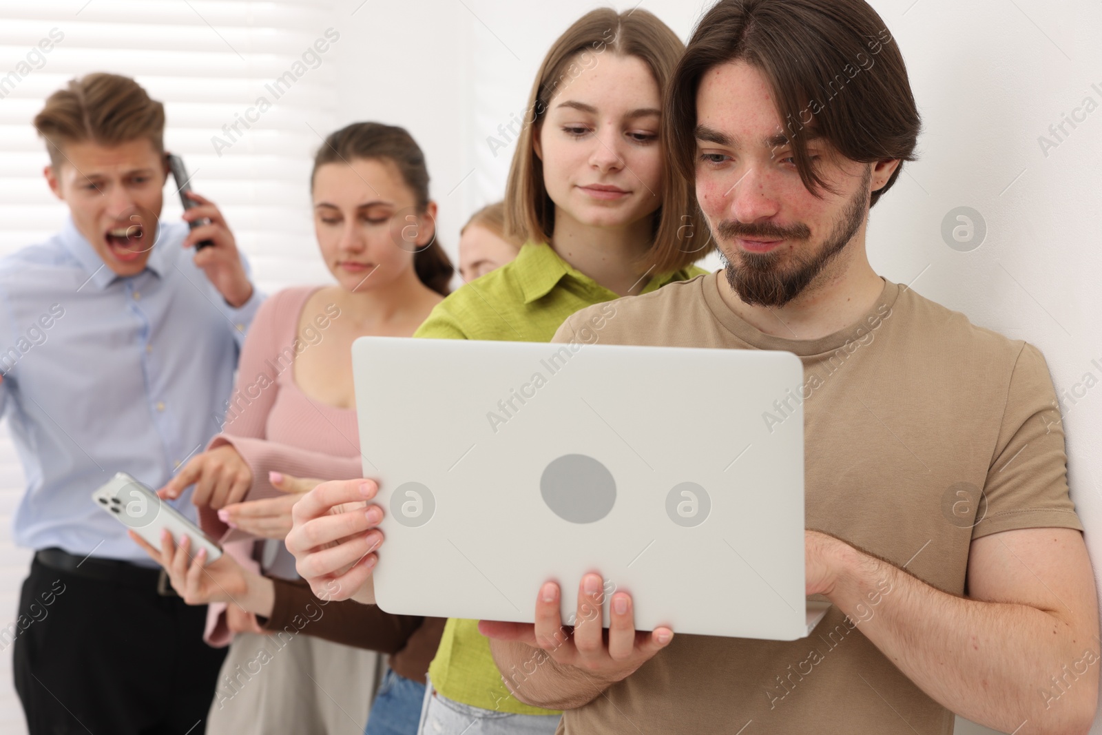 Photo of People with different devices waiting in queue near white wall indoors