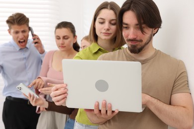 Photo of People with different devices waiting in queue near white wall indoors