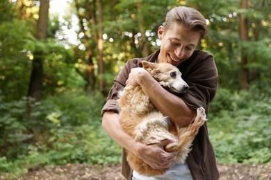 Photo of Happy man holding his cute dog outdoors, space for text