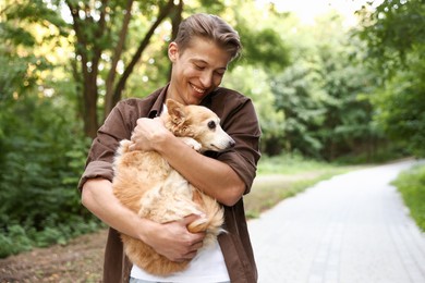 Photo of Happy man holding his cute dog outdoors, space for text