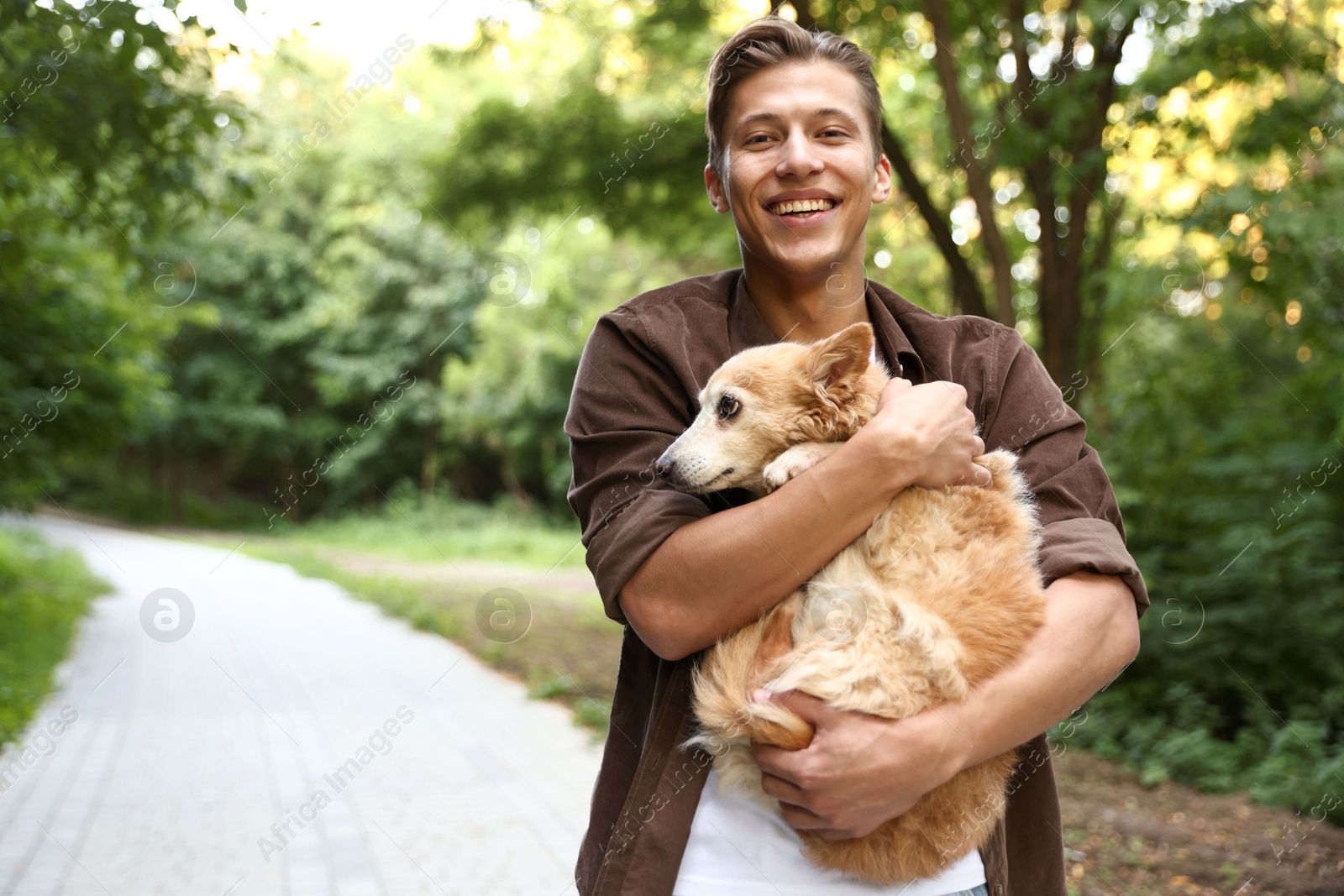 Photo of Happy man holding his cute dog outdoors, space for text