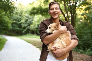 Photo of Happy man holding his cute dog outdoors, space for text