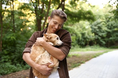 Photo of Happy man holding his cute dog outdoors, space for text