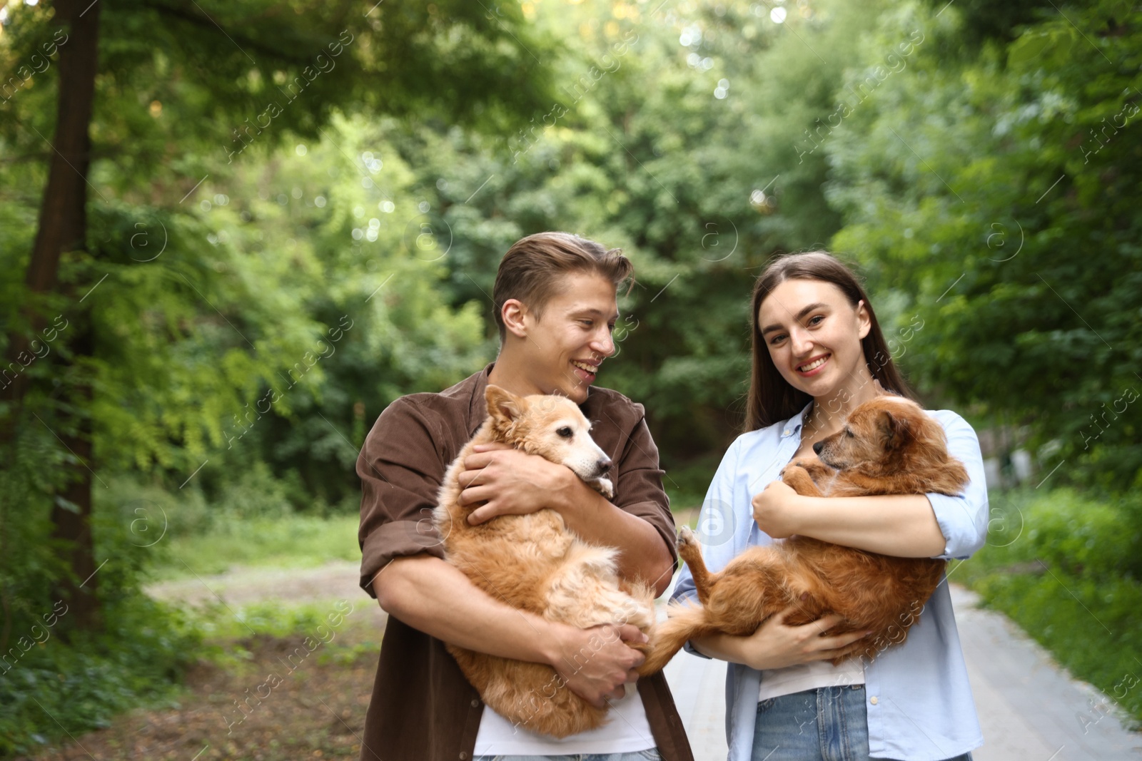Photo of Happy couple holding their cute dogs outdoors, space for text