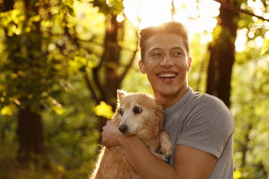 Photo of Happy man holding his cute dog outdoors, space for text