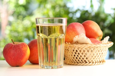 Photo of Delicious cider in glass and apples on white wooden table outdoors