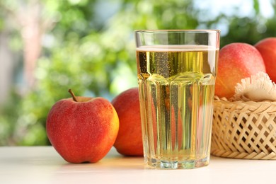 Photo of Delicious cider in glass and apples on white wooden table outdoors, closeup