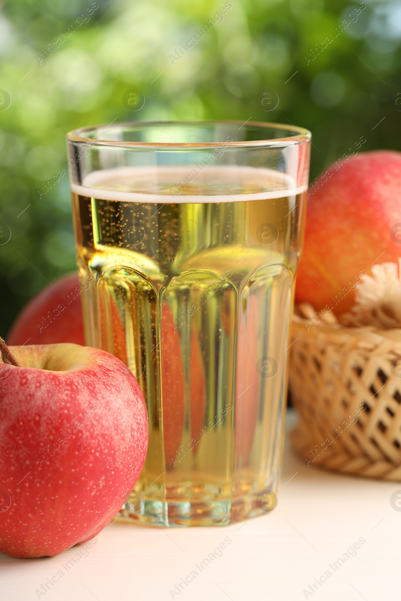 Delicious cider in glass and apples on white wooden table outdoors, closeup Photo of Delicious cider in glass and apples on white wooden table outdoors, closeup