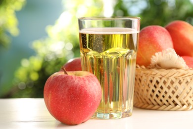 Photo of Delicious cider in glass and apples on white wooden table outdoors, closeup
