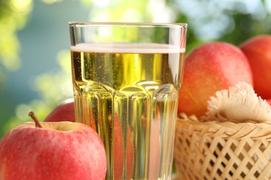 Photo of Delicious cider in glass and apples on blurred background, closeup