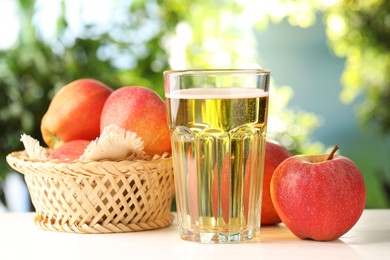 Photo of Delicious cider in glass and apples on white wooden table outdoors