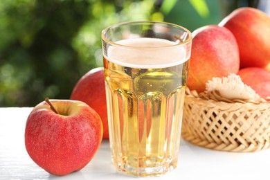 Photo of Delicious cider in glass and apples on white wooden table outdoors, closeup