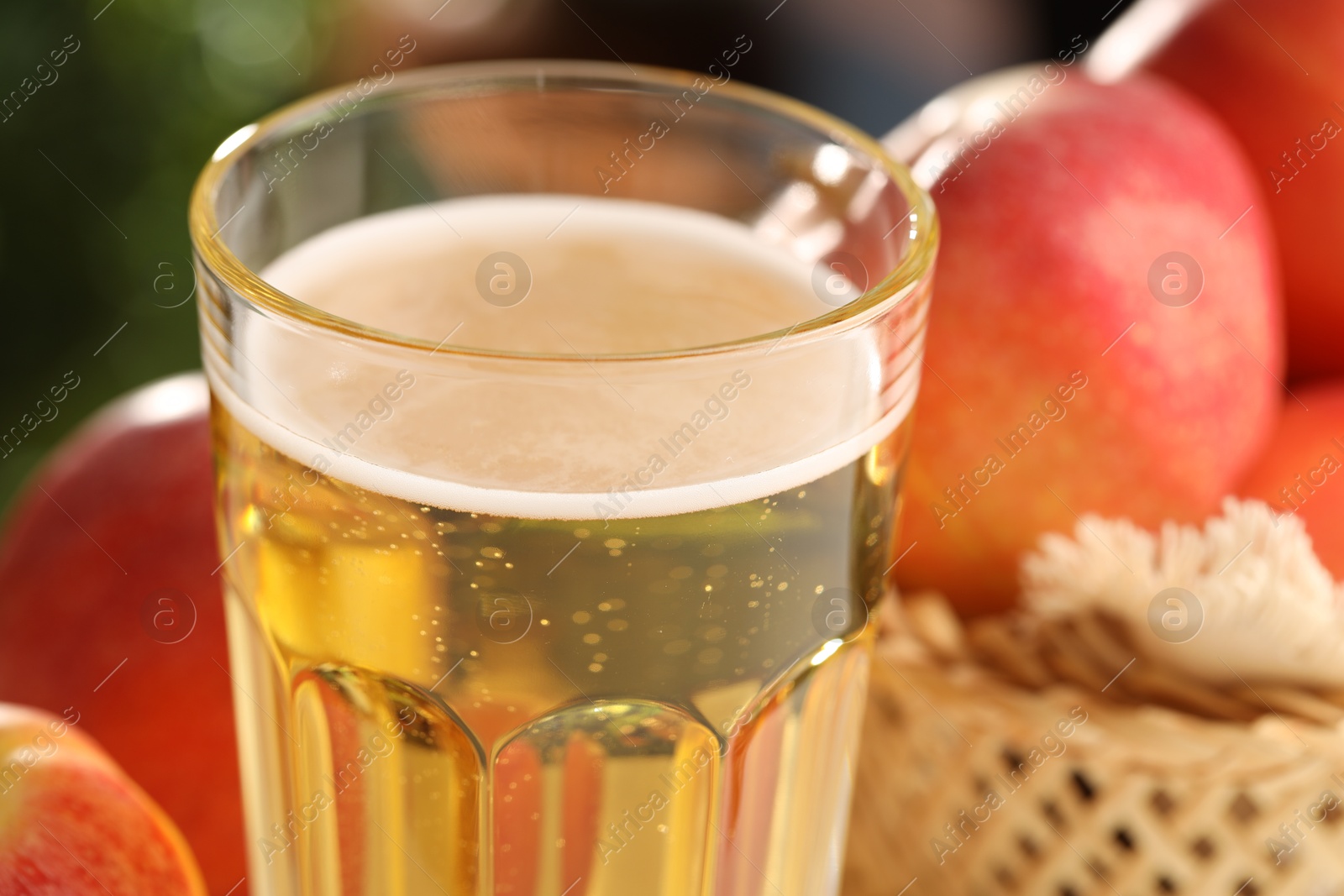Delicious cider in glass and apples on blurred background, closeup Photo of Delicious cider in glass and apples on blurred background, closeup
