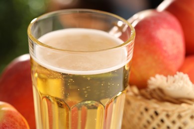 Photo of Delicious cider in glass and apples on blurred background, closeup