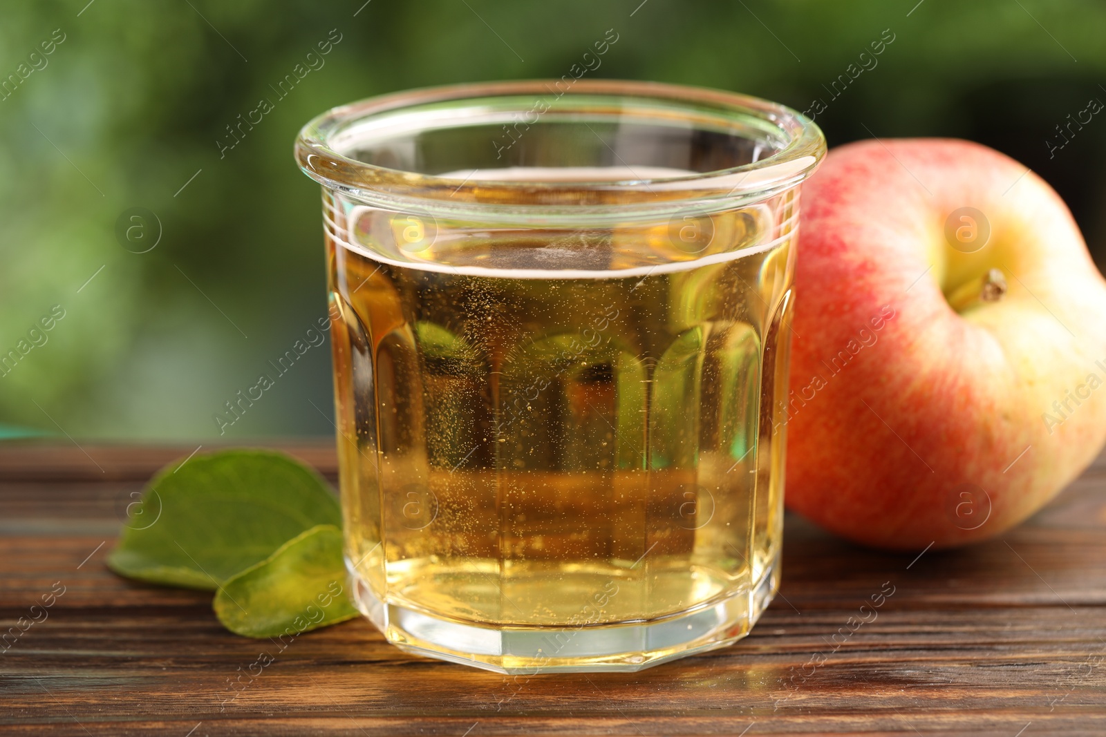 Delicious cider in glass, apple and green leaves on wooden table outdoors, closeup Photo of Delicious cider in glass, apple and green leaves on wooden table outdoors, closeup