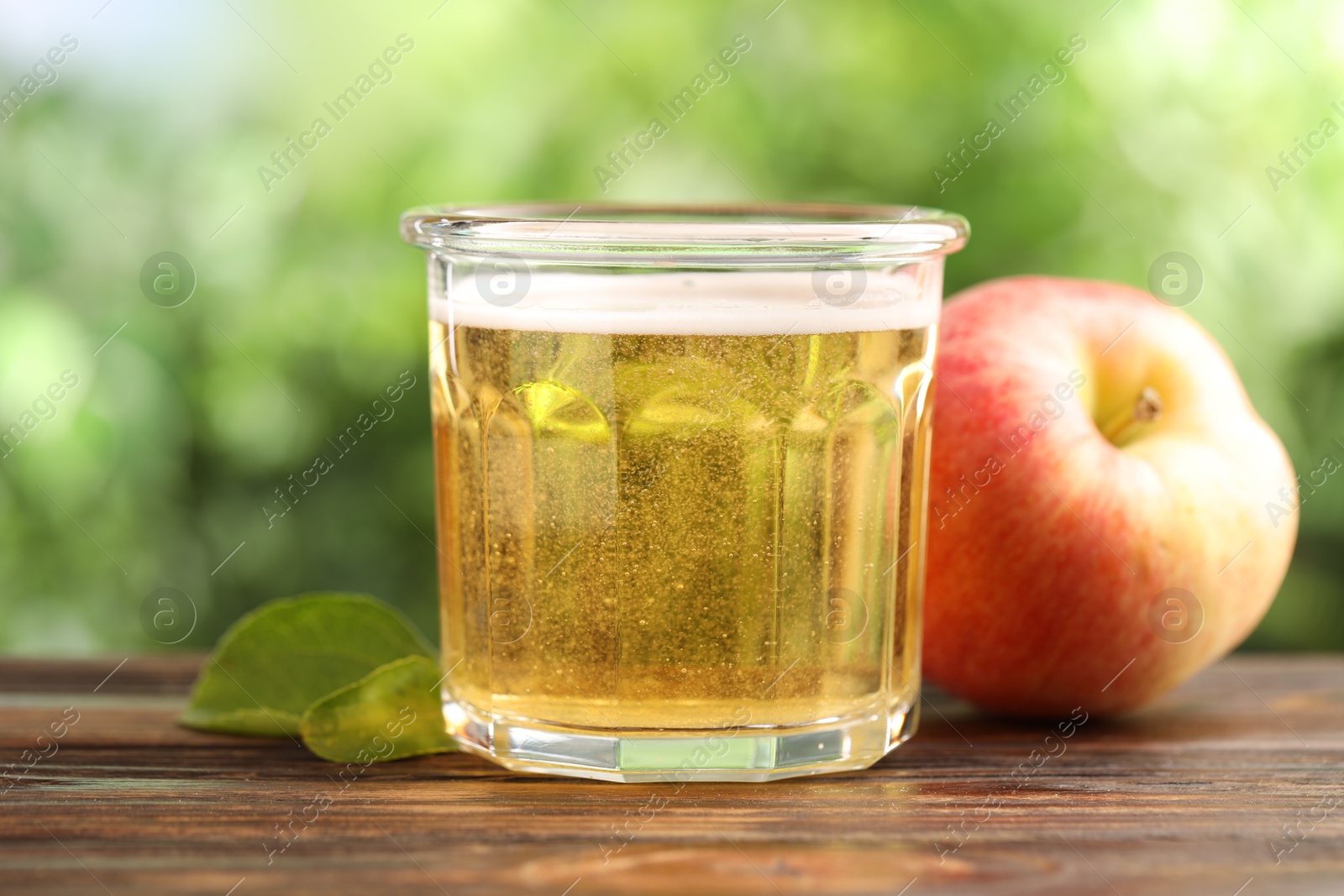 Delicious cider in glass, apple and green leaves on wooden table outdoors, closeup Photo of Delicious cider in glass, apple and green leaves on wooden table outdoors, closeup