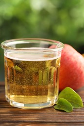 Photo of Delicious cider in glass, apple and green leaves on wooden table outdoors, closeup