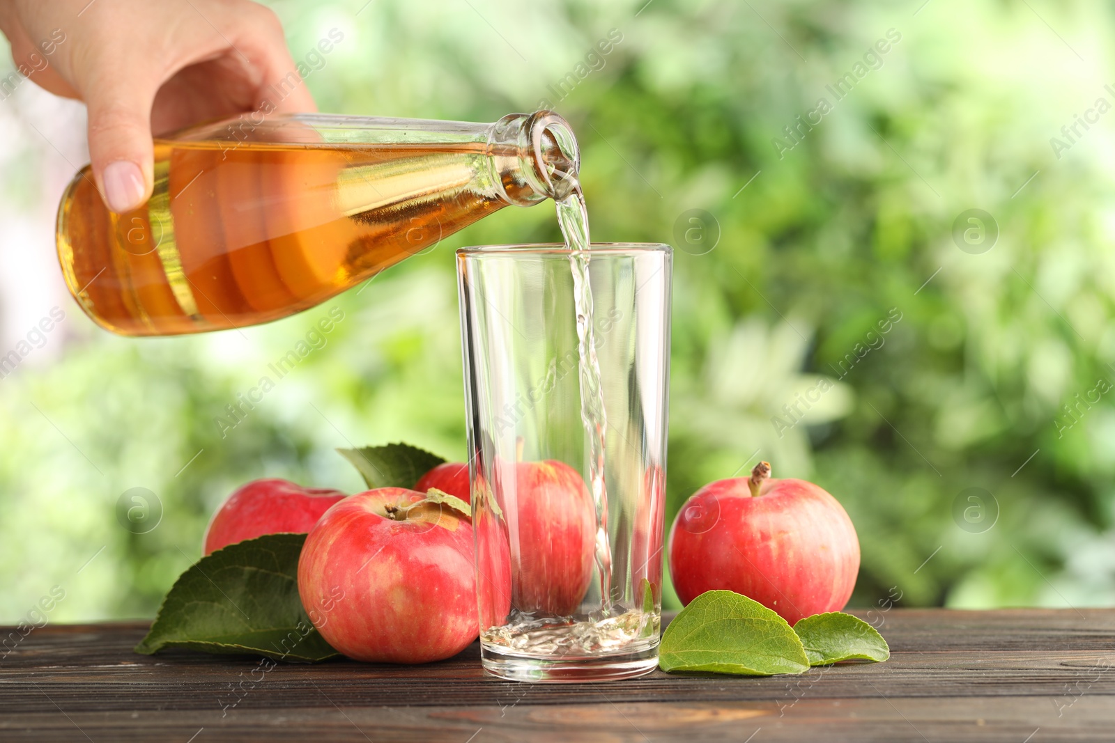 Woman pouring delicious cider into glass at wooden table outdoors, closeup Photo of Woman pouring delicious cider into glass at wooden table outdoors, closeup