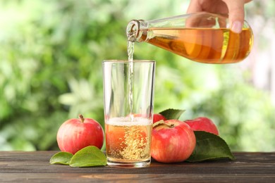 Photo of Woman pouring delicious cider into glass at wooden table outdoors, closeup