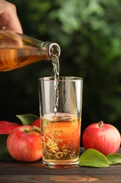 Photo of Woman pouring delicious cider into glass at wooden table outdoors, closeup