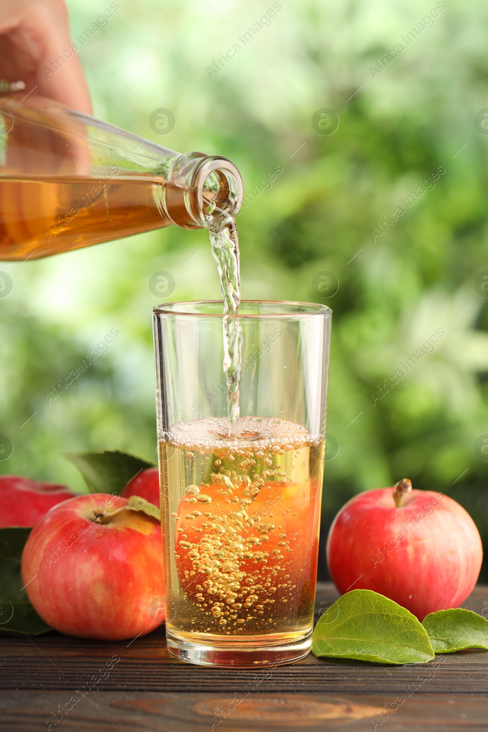 Woman pouring delicious cider into glass at wooden table outdoors, closeup Photo of Woman pouring delicious cider into glass at wooden table outdoors, closeup