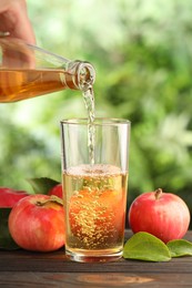 Photo of Woman pouring delicious cider into glass at wooden table outdoors, closeup
