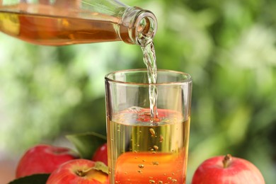 Photo of Pouring delicious cider into glass against blurred background, closeup