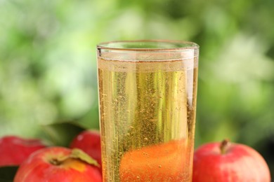Photo of Delicious cider in glass and apples on blurred background, closeup