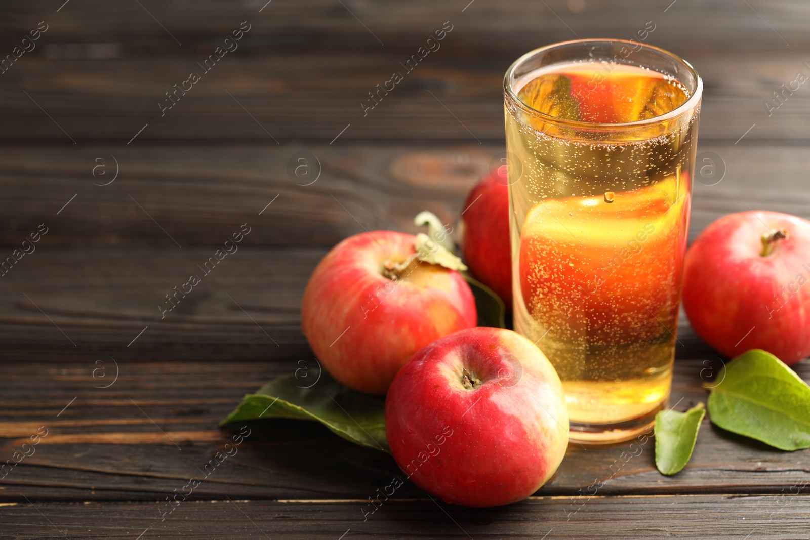 Delicious cider in glass, apples and green leaves on wooden table, closeup. Space for text Photo of Delicious cider in glass, apples and green leaves on wooden table, closeup. Space for text