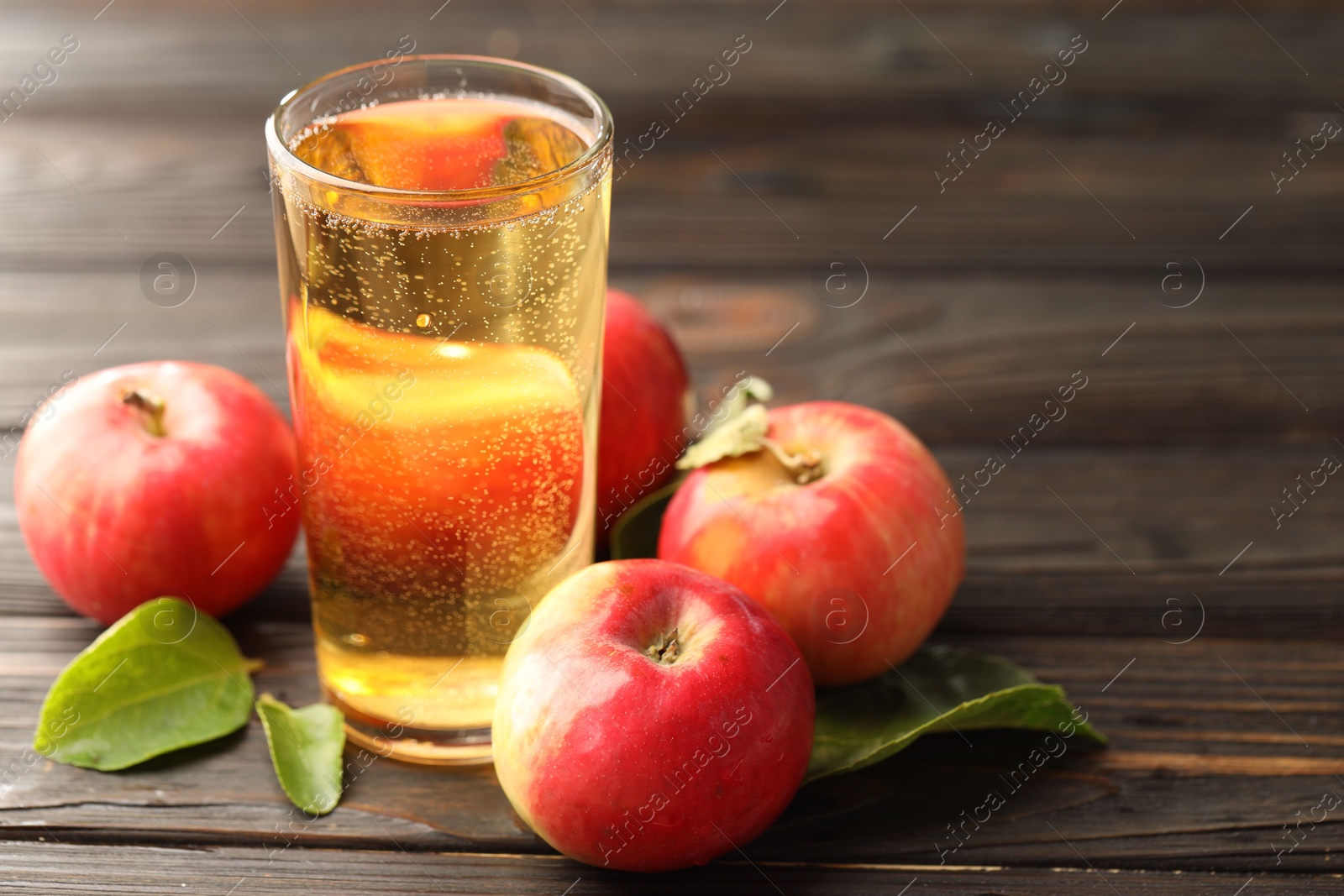 Delicious cider in glass, apples and green leaves on wooden table, closeup. Space for text Photo of Delicious cider in glass, apples and green leaves on wooden table, closeup. Space for text