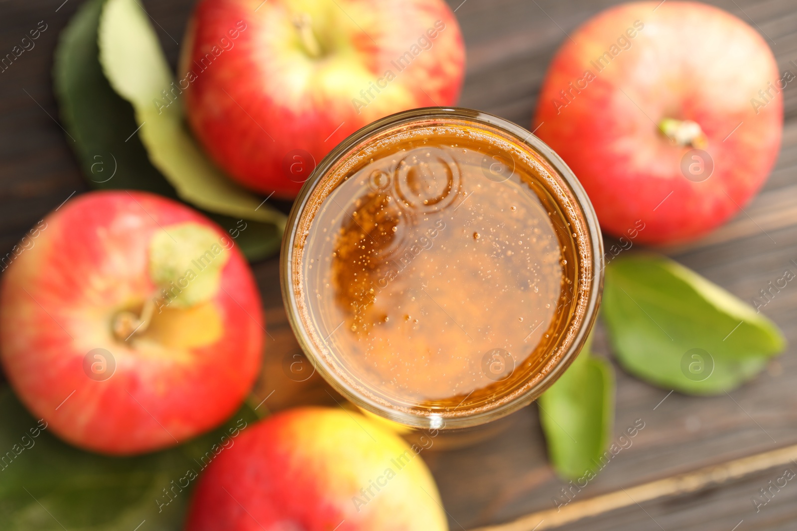 Photo of Delicious cider in glass, apples and green leaves on wooden table, flat lay