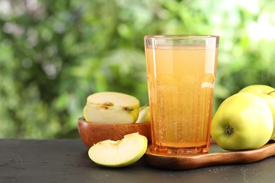 Photo of Delicious cider in glass and apples on black table outdoors, closeup. Space for text