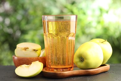Photo of Delicious cider in glass and apples on black table outdoors, closeup