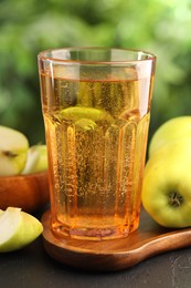Photo of Delicious cider in glass and apples on black table outdoors, closeup