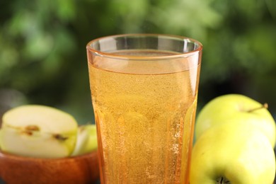Photo of Delicious cider in glass and apples on blurred background, closeup