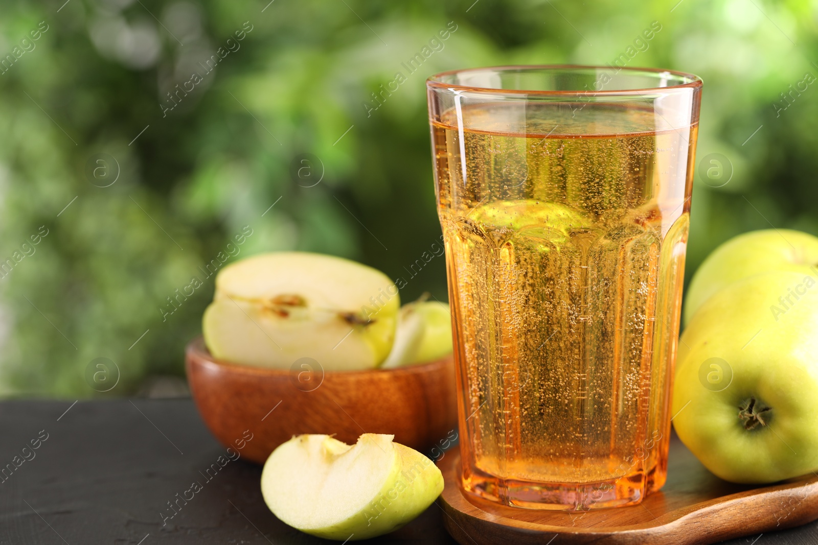 Delicious cider in glass and apples on black table outdoors, closeup Photo of Delicious cider in glass and apples on black table outdoors, closeup
